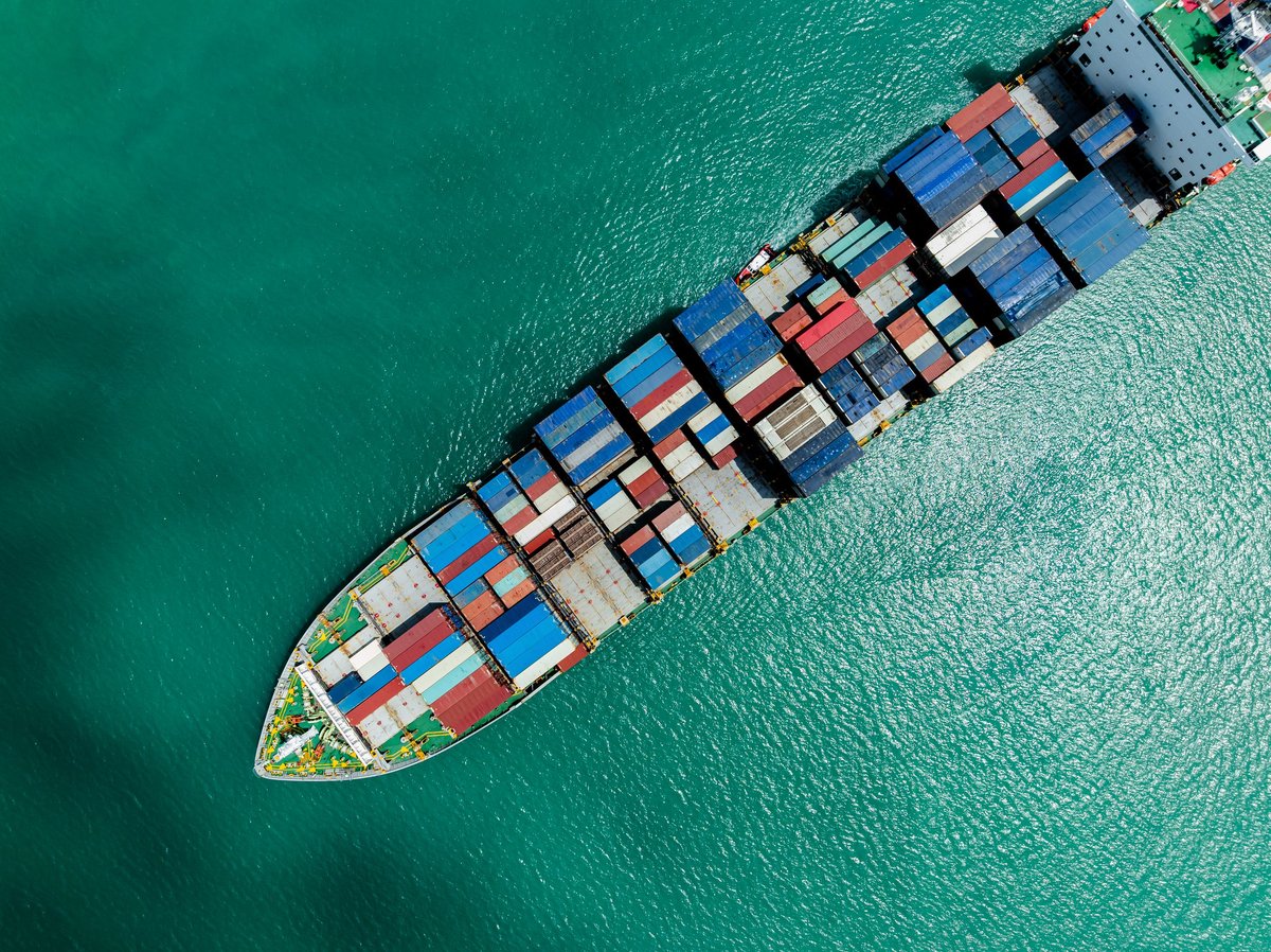 Aerial view of a massive freighter laden with shipping containers cruising through open sea reflecting global supply chain connectivity and maritime logistics in southeast asia.